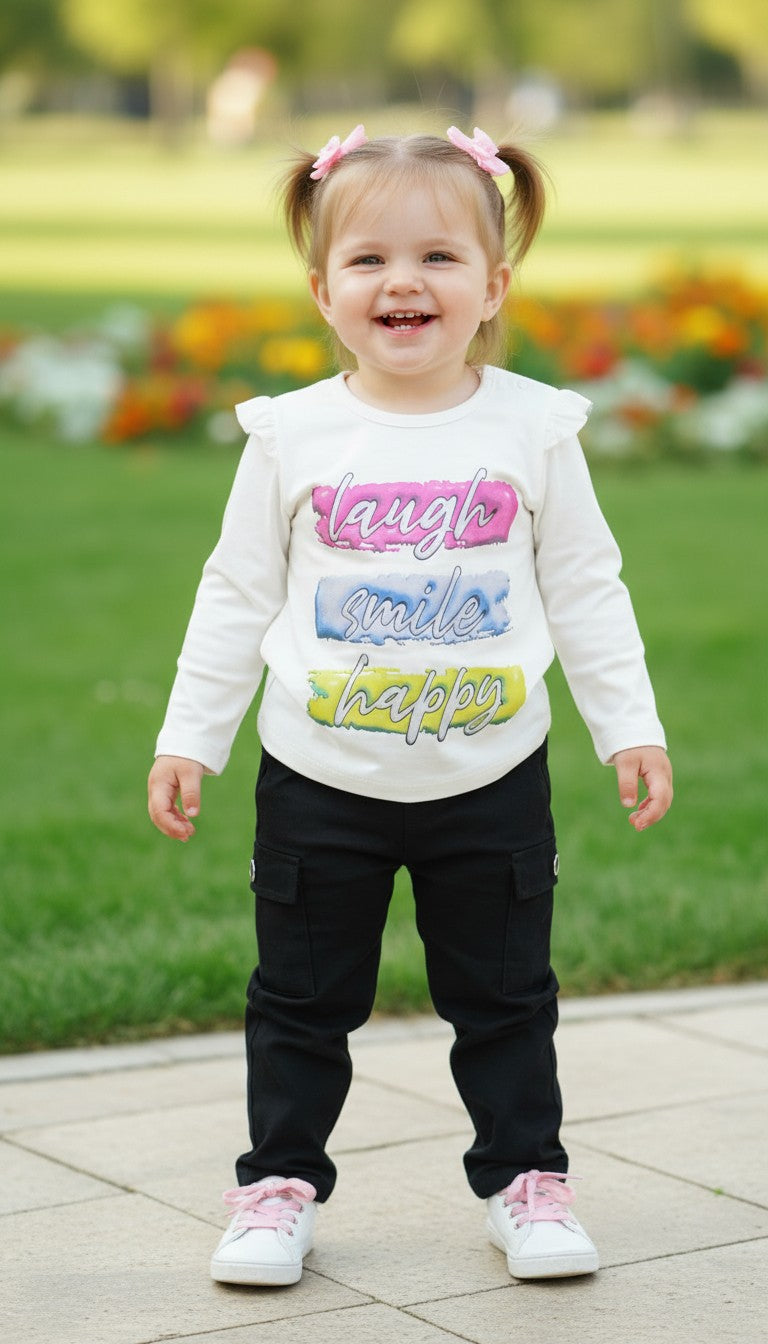 AllurifyYou toddler wearing a white long-sleeved graphic top with ruffle shoulders and black trousers in a park.